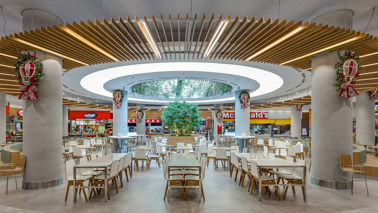 Shopping Mueller, Curitiba. Remodelação da praça de alimentação. A criação de três ambientes com identidades próprias, oferecem maior conforto e diferentes possibilidades de uso ao longo do dia. Destaque para o único ponto de entrada de luz natural que foi marcado com linhas curvas e uma grande jabuticabeira como ponto focal. Projeto premiado na Abrasce 2018 / Expansão e Revitalização. Projetado executado pela espaçonovo arquitetura, empresa especializada em arquitetura de varejo, sediada em São Paulo e qual a arquiteta Jovita Torrano é diretora e fundadora.